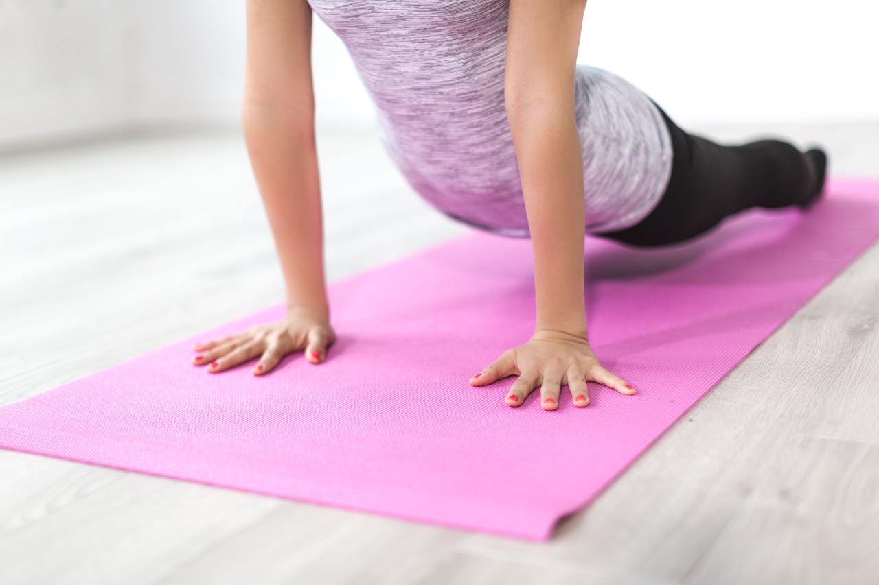 A woman performs a yoga stretch indoors on a pink mat, promoting a healthy lifestyle.