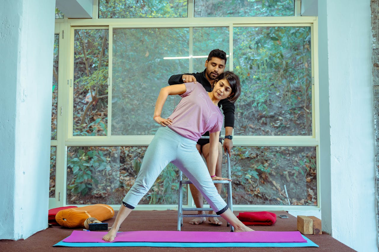 Yoga student stretching with instructor assistance in Rishikesh studio.