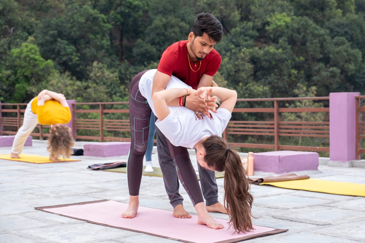 Yoga instructor helps a student with a pose outdoors. Group session amidst nature.